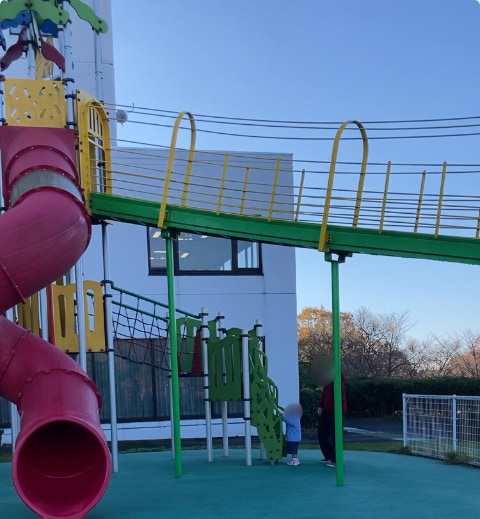 長い滑り台のある大型遊具に小さな子どもが登ろうとしている
