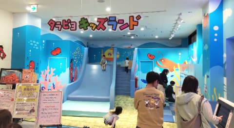 水色で幅の広い大きな滑り台があり、子ども数人がそばで遊んでいる