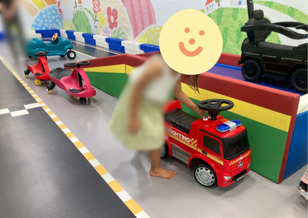 消防車型のミニカーの傍らに子どもが立っている
