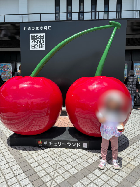 さくらんぼのモニュメントの前に少女が立っている